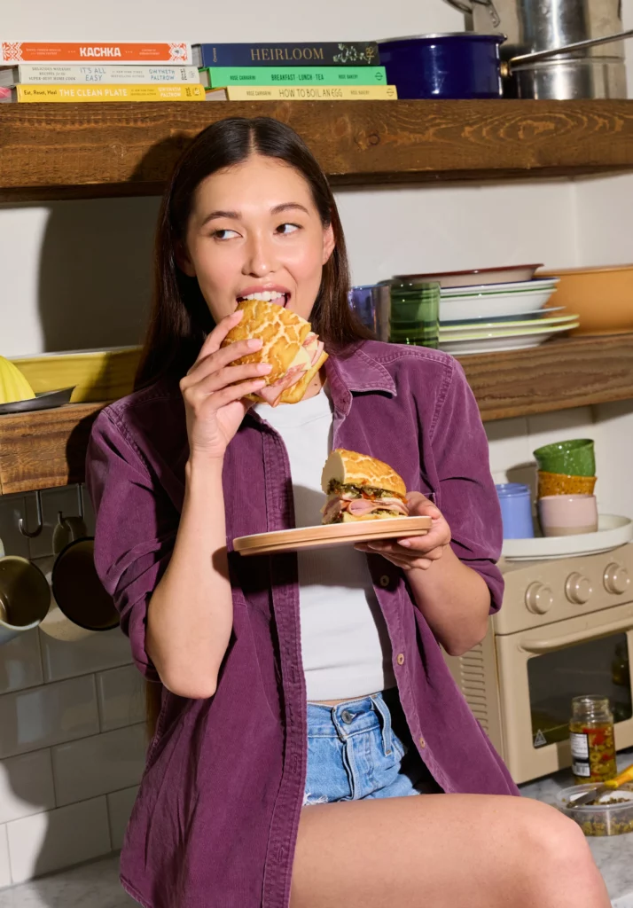Attractive girl in a purple shirt and short sexy jeans eating a Dutch Crunch Sando Sandwich